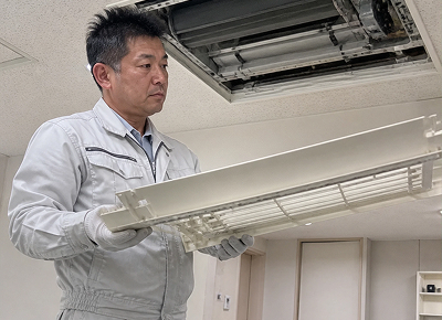 天井埋込みエアコンのパネルを取り外して清掃するスタッフ