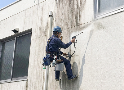 ロープ作業で建物の外壁を高圧洗浄する作業員