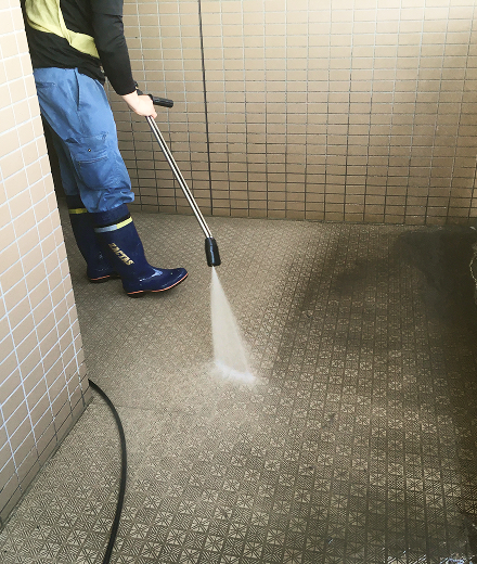 施工中：高圧洗浄機で屋外床面のタイルを洗浄する作業員