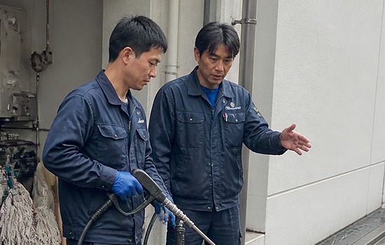 使い方指導：高圧洗浄機のガンの扱い方を先輩スタッフが指導する様子